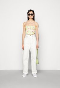Top cropped floral sem alças nas cores amarelo pastel, rosa e verde; calças brancas de perna larga de cintura alta; bolsa verde; óculos de sol pretos.