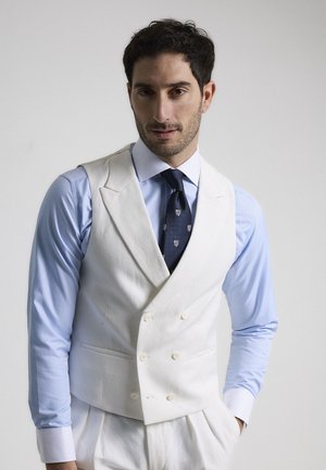 Chaleco blanco de doble botonadura con una textura suave, llevado sobre una camisa celeste y una corbata oscura con un patrón. Diseño sencillo y a medida.