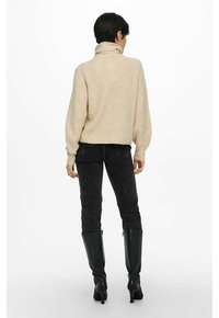 Beige gebreide trui met een hoge kraag, gecombineerd met donkerdenim jeans en knielange zwarte laarzen. Gestructureerde stof en een relaxte pasvorm.