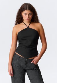 Mustapaitapusero, jossa on hieman teksturoitu pinta ja vino helma, yhdistettynä tummanharmaisiin, teksturoituihin leveisiin housuihin.