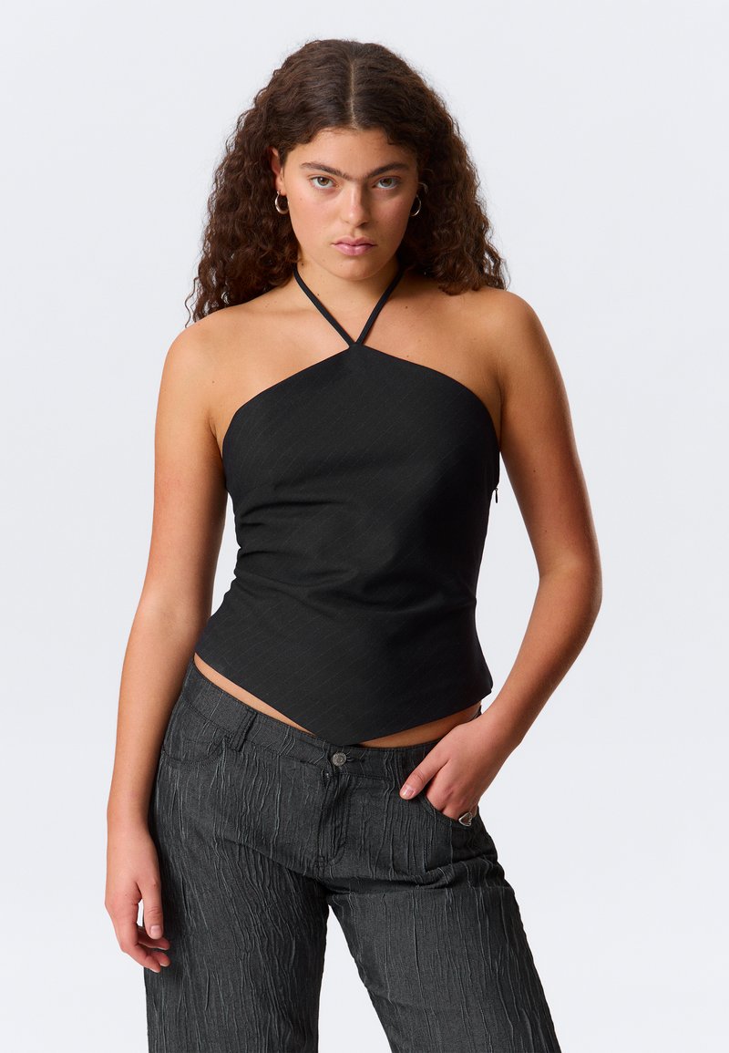 Mustapaitapusero, jossa on hieman teksturoitu pinta ja vino helma, yhdistettynä tummanharmaisiin, teksturoituihin leveisiin housuihin.