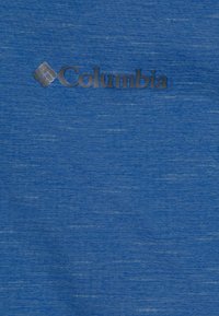 Mėlynas audinys su subtiliu heather stiliumi. Viršuje, centre, yra Columbia logotipas metaline pilka spalva.