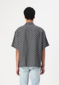 Lyhythihaisessa musta-valkoisessa kuvioidussa paidassa on rento istuvuus, jossa on geometrinen muotoilu ja kauluskdesign.