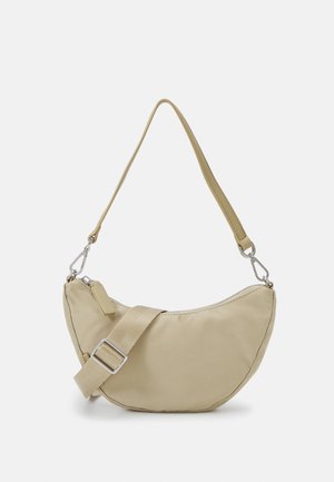 Sac bandoulière beige en forme de croissant avec une large sangle en tissu réglable et une fermeture éclair sur le dessus, sur un fond clair.