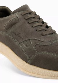 Sneaker in suede verde scuro con punta rotonda, lacci piatti, perforazioni sui lati e una suola beige testurizzata. Branding discreto sul lato.
