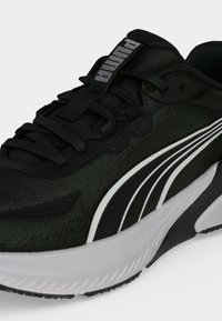 Μαύρο αθλητικό παπούτσι Puma με λευκές καμπυλωτές ρίγες και παχύ λευκό πάτο, με μαύρα κορδόνια και το λογότυπο Puma στη γλώσσα.