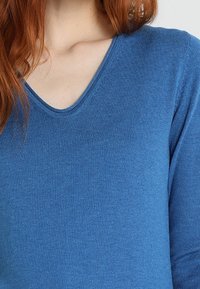 V-ringad mjuk stickad tröja i en livlig blå färg, med en jämn textur och en figurnära design.