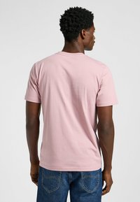 T-shirt rosa chiaro a maniche corte con scollo rotondo e superficie liscia, abbinato a jeans blu. Nessun motivo o accento visibile.