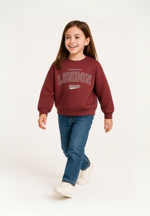 Sweatshirt bordeaux avec le design du texte "LONDON" et "Bienvenue", associé à un jean bleu et des baskets blanches. Tissu doux et coupe décontractée.