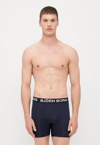 Sötétkék boxer alsónadrág rugalmas anyagból, fekete derékszíjjal, amelyen a "BJÖRN BORG" logó fehér betűkkel látható.
