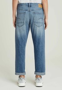 Jeans de mezclilla de color azul claro con un corte relajado, puños enrollados, dos bolsillos traseros y una etiqueta color beige en la cintura. Acabado texturizado.
