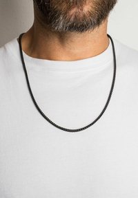 Colier negru din lanț cu un design elegant, torsadat. Purtați peste un tricou alb simplu, scoțând în evidență o textură netedă și o suprafață reflectorizantă.