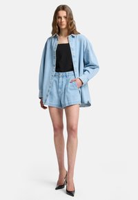 Camicia oversize di denim azzurro chiaro, canotta nera e pantaloni corti di denim abbinati; abbinati a décolleté nere a punta. Vestibilità rilassata, stile casual.