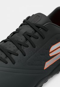 Black athletic shoe with textured upper, gray and orange accents, reinforced toe box, and traditional lacing system.