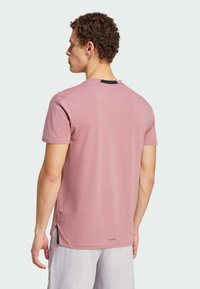 T-shirt rose à manches courtes avec un col rond, présentant des fentes sur les côtés et un accent noir au niveau du col au dos. Tissu doux et texturé.