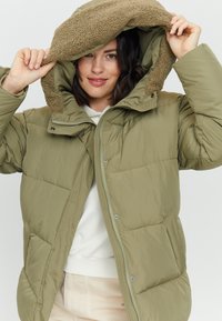 Padded olive green jacket with a textured brown fleece-lined hood, zip closure, and snap buttons; features a quilted design and pockets.