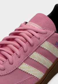 Κοντινό πλάνο ροζ σουέντ αθλητικού παπουτσιού με ροζ κορδόνια, μπεζ ριγέ υφή και καφέ λαστιχένια σόλα.