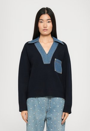 Mekko navy-sininen svetari, jossa on farkku V-pääntie ja etutasku, rento istuvuus ja pitkät hihat. Teksturoitu kangas korostaa kaulan yksityiskohtia.