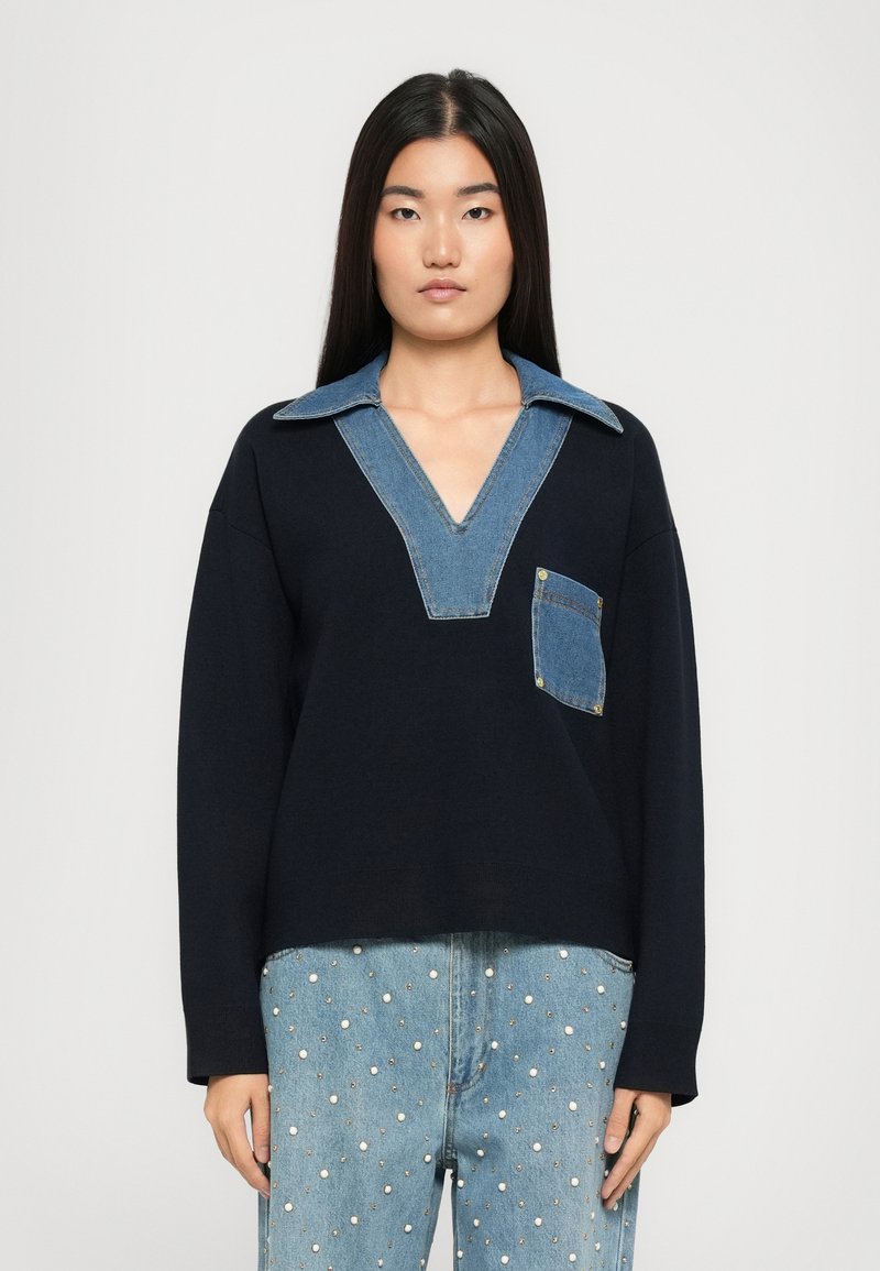 Felpa blu navy con colletto a V in denim e tasca frontale, con una vestibilità rilassata e maniche lunghe. Il tessuto testurizzato contrasta con i dettagli del colletto.