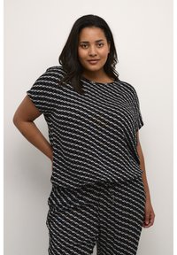 Top nero con una vestibilità ampia e maniche corte, caratterizzato da un motivo geometrico bianco e azzurro chiaro. Abbinato a pantaloni neri con motivo.