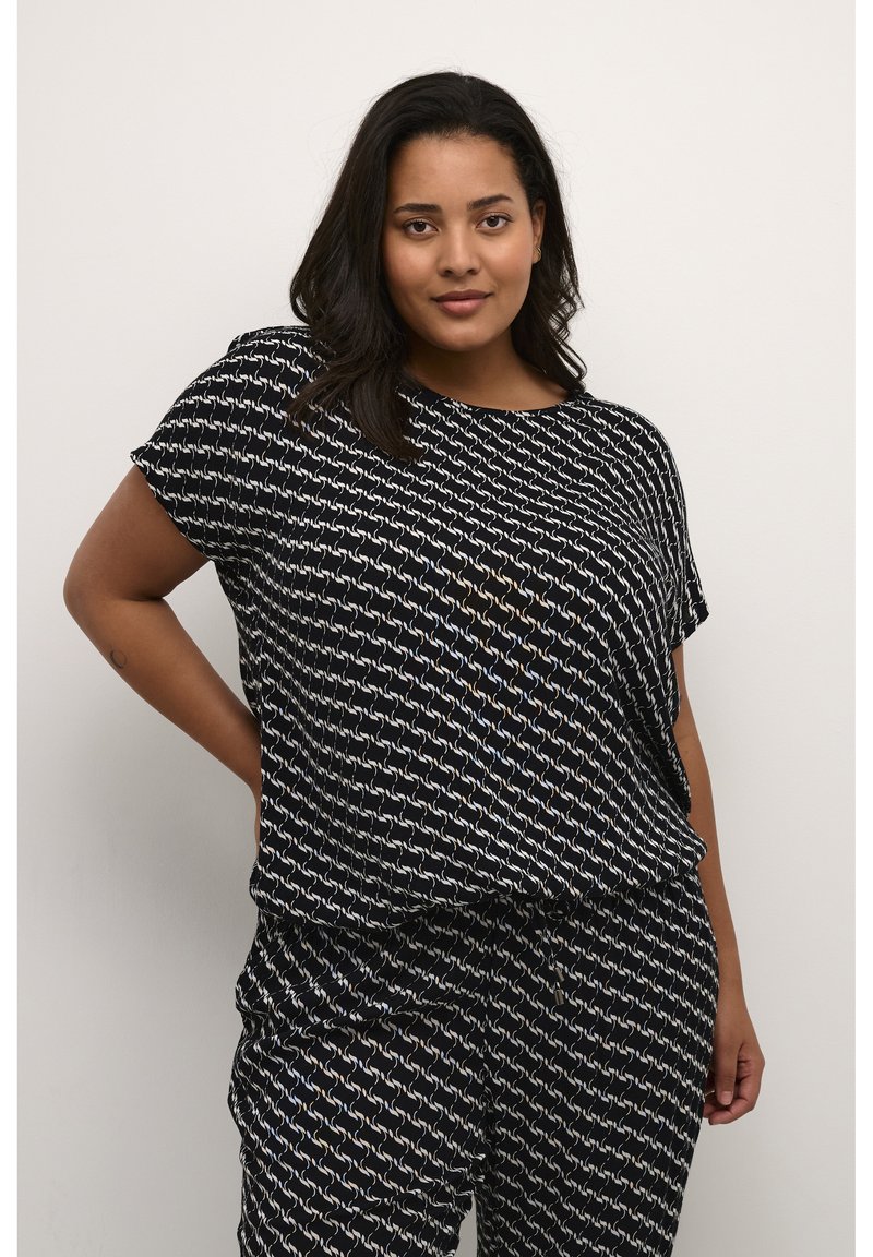 Top nero con una vestibilità ampia e maniche corte, caratterizzato da un motivo geometrico bianco e azzurro chiaro. Abbinato a pantaloni neri con motivo.