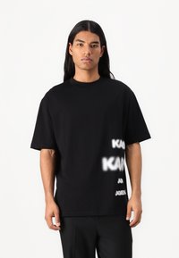 Μαύρη βαμβακερή μπλούζα κοντό μανίκι με γραφικά λευκού χρώματος στο μπροστινό μέρος. Στρογγυλή λαιμόκοψη, χαλαρή γραμμή, λεία υφή.