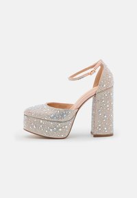 Escarpins beiges à plateforme avec un talon bloc pailleté et épais, ornés de strass et de perles, dotés d'une bride de cheville à boucle.