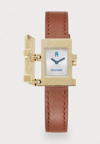 Square gold watch with brown leather strap, hinged cover open, white face displaying blue "TH" logo and "HILFIGER" text, black hands.