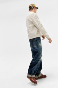 Cremefarvet cable-knit sweater med et struktureret mønster, parret med mørkeblå brede bukser og brune snøresko. Designet til afslappet brug.