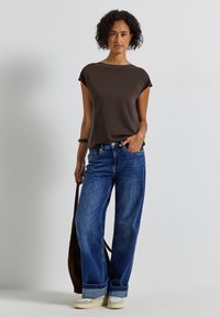 Top court marron à manches courtes associé à un jean en denim bleu à jambes larges. Les jeans présentent un léger revers en bas et un coupe décontractée.