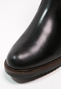 Botte en cuir noir avec un bout arrondi, texture lisse et semelle brune contrastante. Design minimaliste sans hardware ni accents visibles.