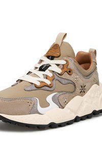 Sneaker beige e grigia con materiali misti, accenti bianchi, suole texturizzate e un dettaglio in pelle marrone sulla linguetta.