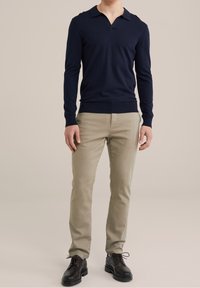 Marinblå stickad tröja med V-ringning och kort krage, i kombination med ljusbeiga slim-fit-byxor och svarta snörskor. Slät textur genomgående.