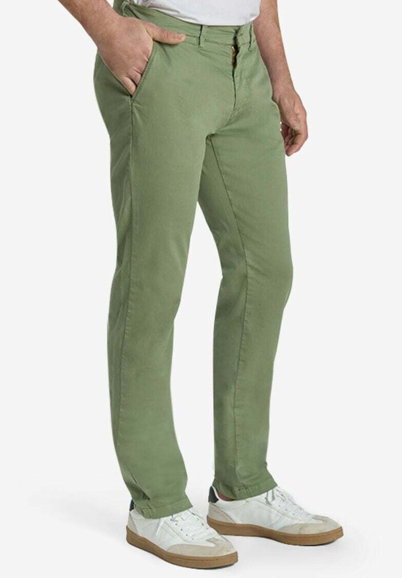 Man draagt lichtgroene slim-fit broek met handen in de zakken en witte sneakers met bruine zolen.