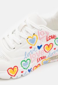 Weiße Sneaker mit bunten Herz- und "Liebe"-Grafiken. Sie haben runde Schnürsenkel, eine glatte Oberfläche und eine strukturierte Verzierung in der Nähe der Sohle.