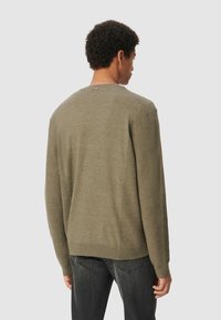 Olivgrüner Pullover mit gerippter Struktur an Ärmeln und Rücken, Rundhalsausschnitt und lockerer Passform. Getragen mit dunklen Jeans.