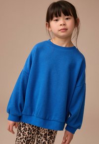 Blaues übergroßes Sweatshirt mit Rundhalsausschnitt und elastischen Bündchen, kombiniert mit Leggings im Leopardenmuster. Weicher Stoff und lockere Passform.