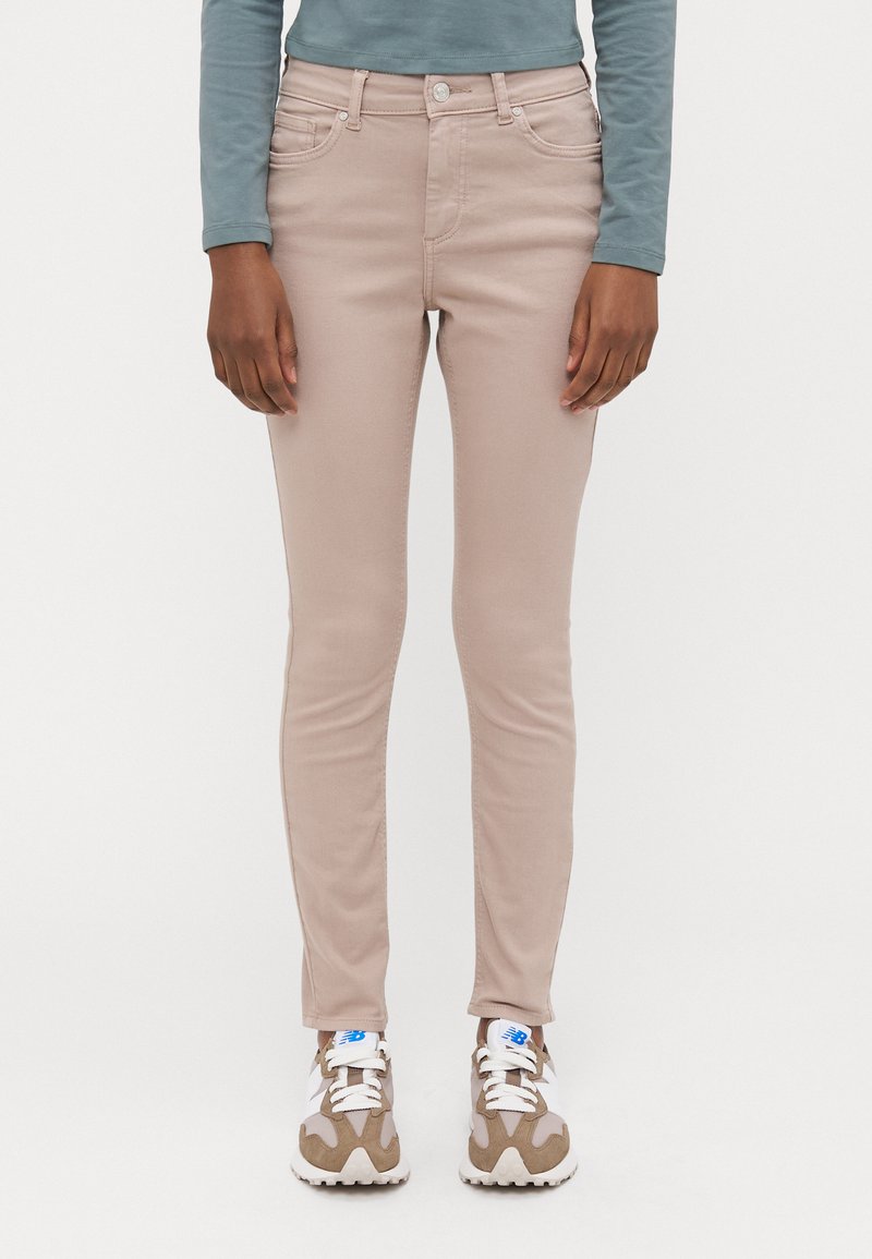Jeans ajustados rosa claro con una textura suave, diseño de cinco bolsillos y herrajes plateados; usados con zapatillas deportivas blancas y beige.