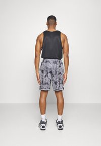 Débardeur noir sans manches, shorts noir et blanc à motif abstrait, accompagnés de chaussettes blanches et de baskets noires.