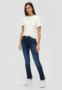 T-shirt blanc à manches courtes associé à un jean slim bleu marine avec des accents déchirés, complété par des baskets blanches.