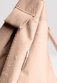 Zaino rosa chiaro con tessuto testurizzato, caratterizzato da gocce d'acqua, una tracolla intrecciata e un accento metallico su un lato.