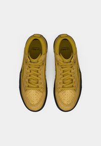 Baskets en daim jaune avec un embout perforé, des lacets plats, un col rembourré et une semelle en caoutchouc noire. Marquage visible sur la languette intérieure.