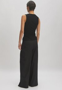 Zwarte geribbelde mouwloze top gecombineerd met losse zwarte wijde broek. Glad stofoppervlak met een eenvoudig ontwerp en zonder versieringen.
