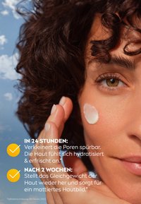 Moisturizing cream applied to the cheek of a woman with curly hair, against a blue sky background. Text includes benefits of the product in German.