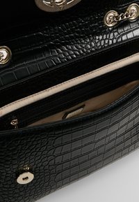 Černá kabelka z umělé kůže s krokodýlím vzorem a zlatými doplňky, obsahující kapsu na zip a béžovou podšívku. Uzavírání na patentní knoflík.