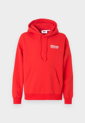 Punane kapuutsiga fliis, valmistatud puuvillasegust, ees tasku, soonikkoes varrukasäärtega ja rinnal logoga. Sile tekstuur.