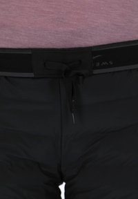 Black padded shorts feature a textured waistband with a black drawstring. The material appears smooth with a sleek design and minimal accents.