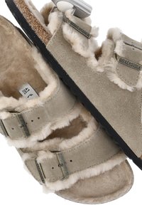 Sandali in suede beige con morbida fodera in pelliccia, due cinturini regolabili, fibbie in metallo e una suola nera texturizzata. Marchiati "Birkenstock."