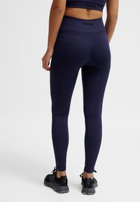 Leggings a vita alta di colore blu navale con texture a coste verticali, realizzati in un materiale elasticizzato, abbinati a scarpe sportive nere.
