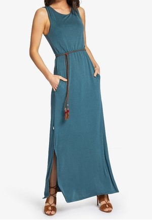 Bezrękawna długia sukienka maxi w kolorze morskim z bocznym rozcięciem, brązowy pleciony pasek z frędzlami, boczne kieszenie, noszona z brązowymi sandałami na obcasie z paseczkami.